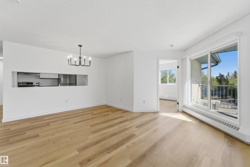Open concept living space featuring wood-finish flooring, a modern chandelier, and a pass-through window to the kitchen - 302 2508 50 Street Nw, Edmonton, AB - Indoor