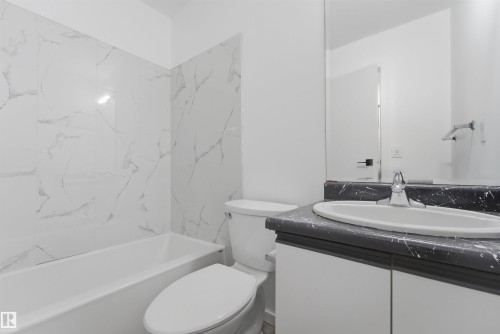 Bathroom featuring a white bathtub, a toilet, a vanity with an integrated sink, a dark countertop, and a large wall mirror - 302 2508 50 Street Nw, Edmonton, AB - Indoor Photo Showing Bathroom