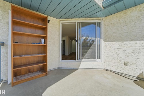 Outdoor concrete patio with a stucco exterior, featuring a sliding glass door with screen, light-colored wood-finish shelving, and a blue plank ceiling - 302 2508 50 Street Nw, Edmonton, AB - Outdoor With Exterior