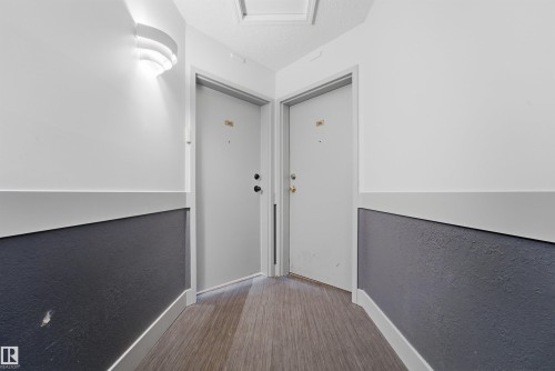 Angled hallway with wood-finish flooring, two-tone walls with a dark lower section, and two white doors - 302 2508 50 Street Nw, Edmonton, AB - Indoor Photo Showing Other Room