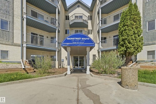 Multi-story building entrance featuring a blue awning, glass double doors, and multiple balconies with metal railings - 302 2508 50 Street Nw, Edmonton, AB - Outdoor With Facade