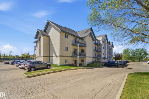 Multi-level stucco exterior building featuring balconies with metal railings, a gabled roofline with dark shingles, and surrounding green spaces - 302 2508 50 Street Nw, Edmonton, AB - Outdoor