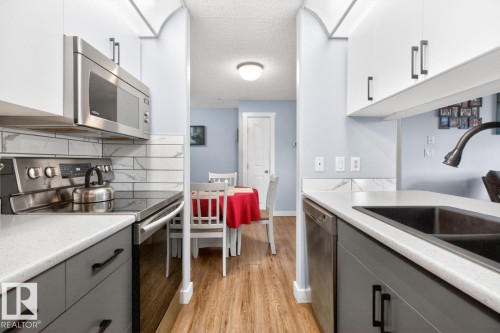 Modern kitchen featuring stainless steel appliances, solid surface countertops, a mosaic tile backsplash, and two-tone cabinetry with black hardware - 220 16303 95 Street, Edmonton, AB - Indoor Photo Showing Kitchen