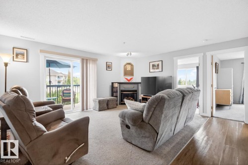 Spacious living area featuring carpet flooring, a built-in fireplace with mantel, and track lighting - 220 16303 95 Street, Edmonton, AB - Indoor Photo Showing Living Room With Fireplace