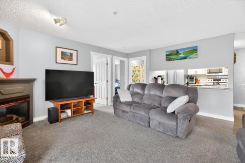 Neutral gray walls complement the textured gray carpeting in this living area, featuring a built-in electric fireplace with a dark wood mantel - 220 16303 95 Street, Edmonton, AB - Indoor Photo Showing Living Room With Fireplace