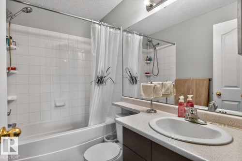 Bathroom featuring a white subway tile shower surround with a tub, a built-in vanity with a composite countertop, an oval undermount sink, and a large wall-mounted mirror - 220 16303 95 Street, Edmonton, AB - Indoor Photo Showing Bathroom