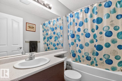 Bathroom featuring a white vanity with an integrated sink, a full-width mirror, and a white bathtub with white subway tile surround - 220 16303 95 Street, Edmonton, AB - Indoor Photo Showing Bathroom
