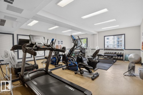 Fitness center with cardio equipment, mirrored wall, dumbbell rack, and large window - 220 16303 95 Street, Edmonton, AB - Indoor Photo Showing Gym Room