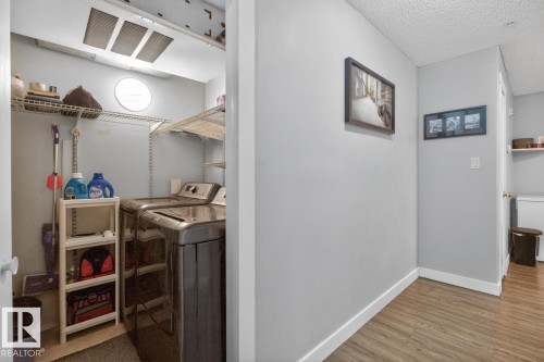 Dedicated laundry area featuring wire shelving, a circular window, and overhead lighting - 220 16303 95 Street, Edmonton, AB - Indoor Photo Showing Laundry Room