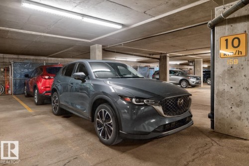 Underground parking area featuring concrete pillars and ceiling, fluorescent lighting, and a painted yellow line designating a parking space - 220 16303 95 Street, Edmonton, AB - Indoor Photo Showing Garage