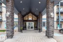 Building entrance featuring stacked stone columns, a covered portico with recessed lighting, and a gabled architectural detail above the glass entry doors - 220 16303 95 Street, Edmonton, AB  - Outdoor With Balcony With Facade 