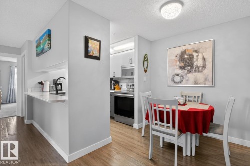 Open-concept dining area with wood-finish flooring, recessed lighting, and a kitchen pass-through featuring a quartz countertop - 220 16303 95 Street, Edmonton, AB - Indoor