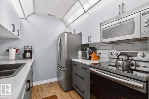 Modern kitchen featuring stainless steel appliances, a double basin sink, light grey countertops, and wood-finish flooring - 220 16303 95 Street, Edmonton, AB - Indoor Photo Showing Kitchen With Double Sink