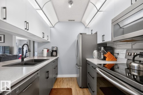 Modern kitchen featuring a dual-tone cabinetry design, wood-finish flooring, stainless steel appliances, a black double-basin sink with a matte black faucet, and a subway tile backsplash - 220 16303 95 Street, Edmonton, AB - Indoor Photo Showing Kitchen With Double Sink With Upgraded Kitchen