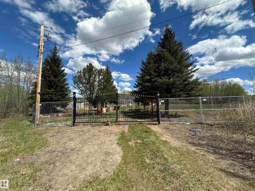 Fenced perimeter featuring a black wrought iron gate and chain-link fencing, mature evergreen trees, and a gravel driveway - #41 59419 Rge Rd 240, Rural Westlock County, AB - Outdoor With View