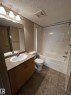 Full bathroom featuring a vanity with integrated sink, a rectangular mirror, overhead vanity lighting, a full bathtub with shower, and tiled flooring - 205 11445 Ellerslie Road, Edmonton, AB 