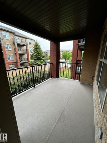 Private balcony featuring a concrete floor, black metal railings, and a dark paneled ceiling - 205 11445 Ellerslie Road, Edmonton, AB 