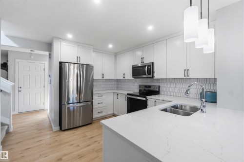 Modern kitchen featuring white cabinetry with dark hardware, stainless steel appliances, and a light-toned wood-finish flooring - 5129 Lark Crescent, Edmonton, AB - Indoor Photo Showing Kitchen With Double Sink With Upgraded Kitchen