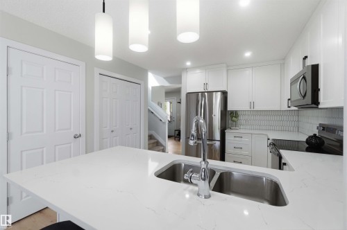 Kitchen featuring white cabinetry, stainless steel appliances, a dual basin sink, and pendant lighting - 5129 Lark Crescent, Edmonton, AB - Indoor Photo Showing Kitchen With Double Sink With Upgraded Kitchen