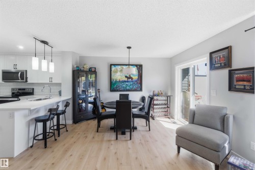 Open-concept living space featuring wood-finish flooring, a contemporary kitchen, a dedicated dining area, modern pendant lighting, and a glass sliding door - 5129 Lark Crescent, Edmonton, AB - Indoor