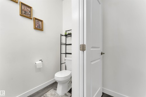 Powder room featuring a white toilet, contemporary dark wood-finish flooring, white baseboards, and a modern interior door with brushed nickel hardware - 22534 98A Avenue, Edmonton, AB - Indoor Photo Showing Bathroom
