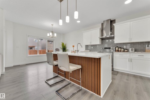 Contemporary kitchen featuring a large central island with slatted wood-finish paneling, white countertops, and pendant lighting - 22534 98A Avenue, Edmonton, AB - Indoor Photo Showing Kitchen With Upgraded Kitchen