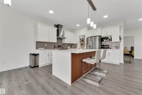 Contemporary kitchen featuring a large central island with seating, white shaker cabinetry, stainless steel appliances, and wood-finish flooring - 22534 98A Avenue, Edmonton, AB - Indoor Photo Showing Kitchen With Upgraded Kitchen