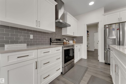 Contemporary kitchen featuring white cabinetry, light countertops, gray subway tile backsplash, stainless steel appliances, and wood-finish flooring - 22534 98A Avenue, Edmonton, AB - Indoor Photo Showing Kitchen With Upgraded Kitchen