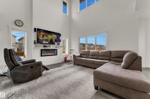 High ceilings with upper windows, integrated wall-mounted electric fireplace, built-in media shelf, and wood-finish flooring - 22534 98A Avenue, Edmonton, AB - Indoor Photo Showing Living Room With Fireplace