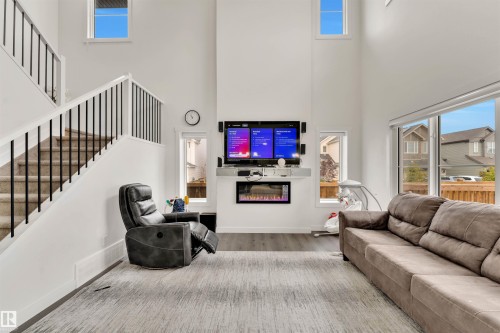 Two-story living area with high ceilings, large windows, wood-finish flooring, a contemporary electric fireplace, and a carpeted staircase with black metal spindles - 22534 98A Avenue, Edmonton, AB - Indoor With Fireplace