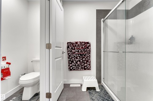 Modern bathroom featuring a glass-enclosed shower with a framed sliding door, grey wall tile accents, and coordinating grey floor tile - 22534 98A Avenue, Edmonton, AB - Indoor Photo Showing Bathroom