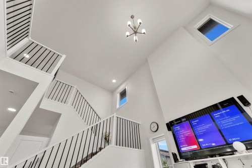 Vaulted ceilings and a contemporary chandelier illuminate a multi-level staircase with white balusters and black metal spindles - 22534 98A Avenue, Edmonton, AB - Indoor Photo Showing Other Room