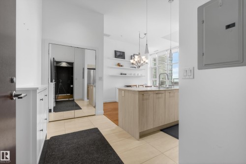 Entry foyer with tile flooring leading to an open-concept kitchen featuring a central island with a sink, pendant lighting, and light wood-finish cabinetry - 808 2612 109 Street, Edmonton, AB - Indoor