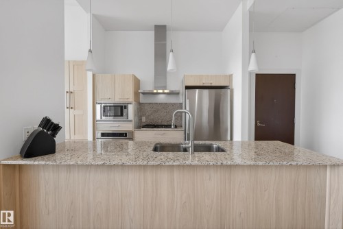 Kitchen featuring a large central island with a double basin sink and a high-arc faucet, light-toned wood-finish cabinetry, stainless steel appliances, and light-colored patterned countertops - 808 2612 109 Street, Edmonton, AB - Indoor Photo Showing Kitchen With Double Sink With Upgraded Kitchen