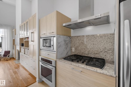 Modern kitchen featuring a gas range, stainless steel appliances, light wood-finish cabinetry, a built-in microwave, and a stone countertop with a matching backsplash - 808 2612 109 Street, Edmonton, AB - Indoor Photo Showing Kitchen