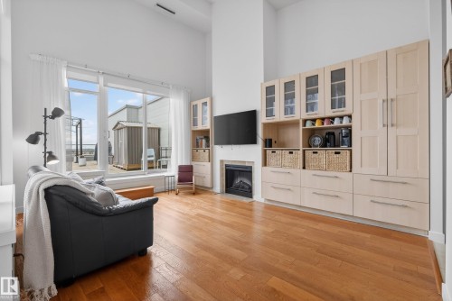 Living space featuring wide plank wood-finish flooring, a built-in media center with integrated fireplace, and expansive sliding glass doors opening to an outdoor patio - 808 2612 109 Street, Edmonton, AB - Indoor With Fireplace