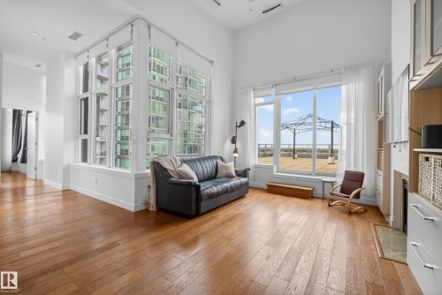 Open-concept living space featuring high ceilings, wood-finish flooring, a full wall of windows with multi-pane architectural details, and an expansive window with outdoor access - 808 2612 109 Street, Edmonton, AB - Indoor Photo Showing Living Room