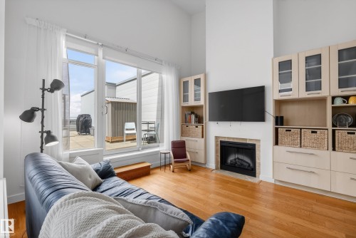 Living area featuring hardwood flooring, a fireplace with stone surround, custom built-in cabinetry, and expansive windows leading to an outdoor patio - 808 2612 109 Street, Edmonton, AB - Indoor Photo Showing Living Room With Fireplace