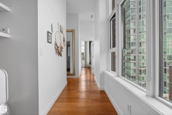 Hallway with wood-finish flooring, white baseboards, and a series of large windows - 