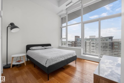 Floor-to-ceiling windows with expansive glass, hardwood flooring, white walls, and a built-in wood-finish cabinet with a white countertop - 808 2612 109 Street, Edmonton, AB - Indoor Photo Showing Bedroom