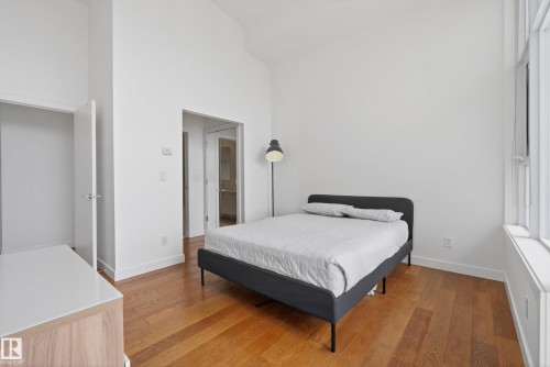 Bright bedroom featuring wood-finish flooring, tall ceilings, and a large multi-pane window - 808 2612 109 Street, Edmonton, AB - Indoor Photo Showing Bedroom