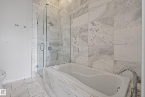 Bathroom featuring a built-in soaking tub with chrome fixtures, a clear glass shower enclosure, and full-height tiled walls - 808 2612 109 Street, Edmonton, AB - Indoor Photo Showing Bathroom