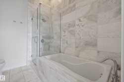 Bathroom featuring a built-in soaking tub with chrome fixtures, a clear glass shower enclosure, and full-height tiled walls - 