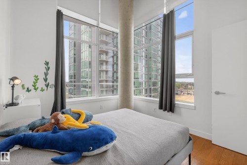 Bedroom featuring expansive window walls, wood-finish flooring, a contemporary white door with brushed nickel hardware, and an exposed concrete column - 808 2612 109 Street, Edmonton, AB - Indoor Photo Showing Bedroom