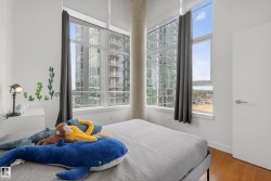 Bedroom featuring expansive window walls, wood-finish flooring, a contemporary white door with brushed nickel hardware, and an exposed concrete column - 