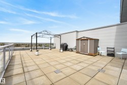 Expansive rooftop patio featuring large format paver tiles, a metal gazebo frame, and a storage shed - 
