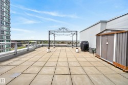 Expansive rooftop patio featuring large format paver flooring, a perimeter glass railing system, and a decorative metal pergola frame - 