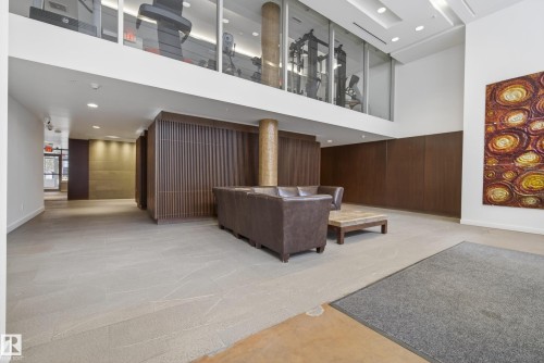 Lobby area featuring a mezzanine-level fitness center with glass paneling, recessed lighting, wood-paneled walls, and light-toned flooring - 808 2612 109 Street, Edmonton, AB - Indoor Photo Showing Other Room
