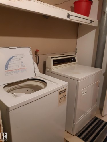 Dedicated laundry area featuring a top-loading washing machine and a front-loading dryer, with an overhead white shelving unit providing storage - 3809 112 Avenue, Edmonton, AB - Indoor Photo Showing Laundry Room