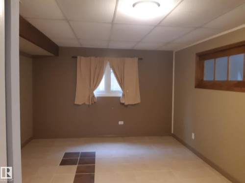 Spacious master bedroom featuring neutral wall tones, square tile flooring with a decorative inlay, a dropped ceiling with recessed lighting, and a window with wood trim - 3809 112 Avenue, Edmonton, AB - Indoor Photo Showing Other Room